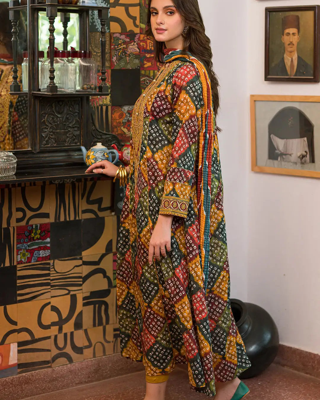 Woman in a colorful traditional outfit standing in a room with decorative walls and framed pictures.