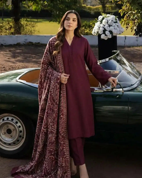 A woman models a three-piece traditional outfit consisting of a deep maroon kurta, matching trousers, and a paisley-patterned dupatta, standing next to a vintage green convertible car.
